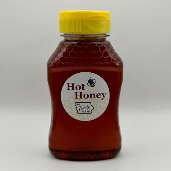 A bottle of BA Family Farms hot honey with a yellow cap and a round white label reading, shown on a light gray background.