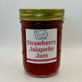 A glass jar of Strawberry Jalapeño Jam with a white label and a gold metal lid, photographed against a plain light gray background.