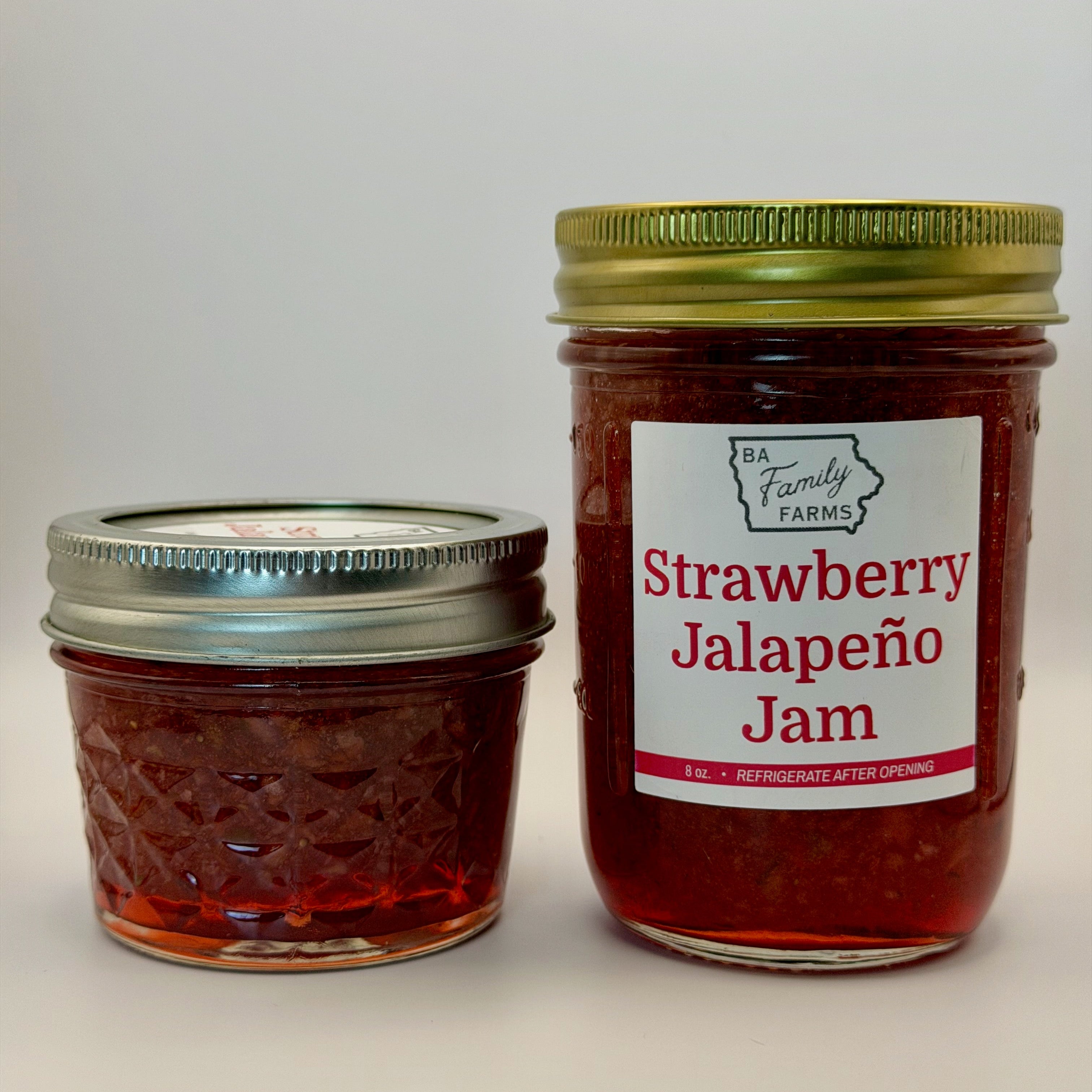 Two glass jars of jam on a light gray background. The larger jar on the right has a white label reading 'Strawberry Jalapeño Jam' with the BA Family Farms.