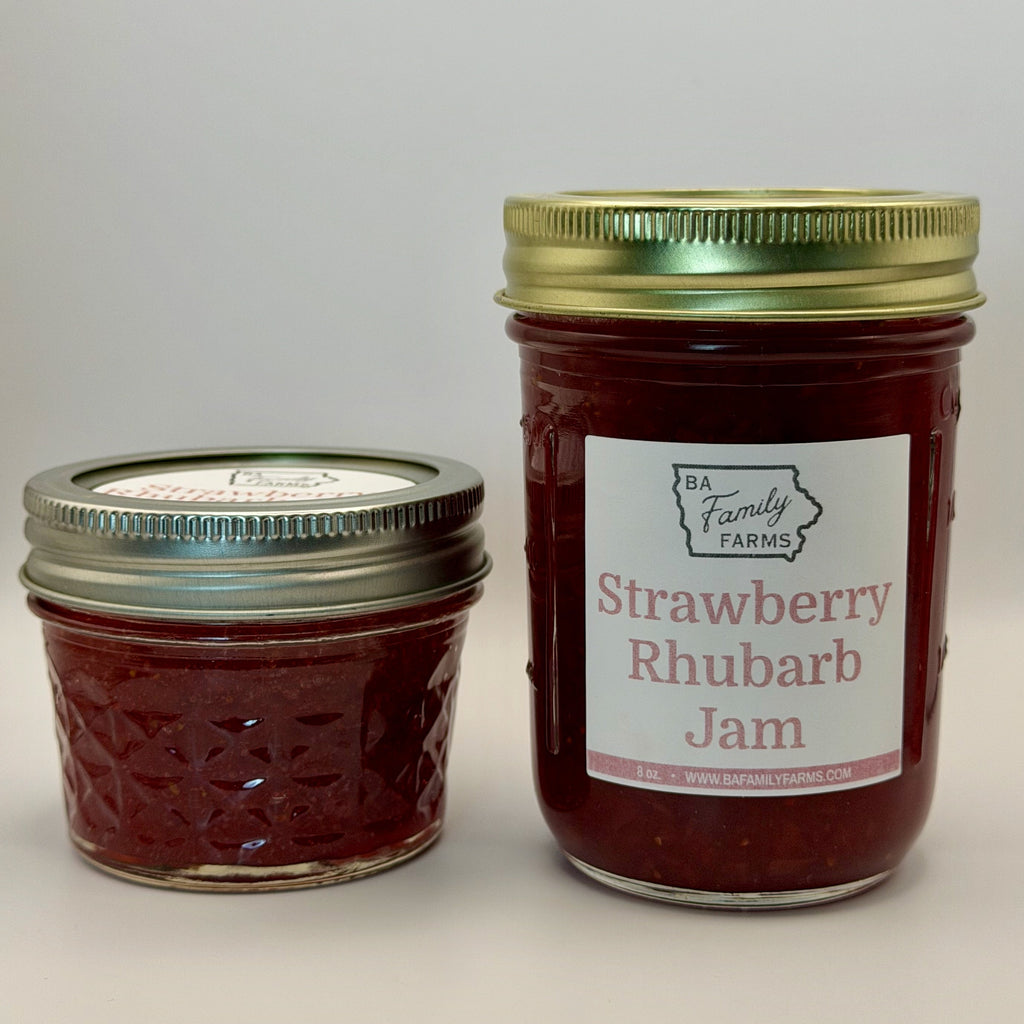 Two glass jars of BA Family Farms Strawberry Rhubarb Jam on a light gray background, with one small jar and one larger jar. The larger jar has a white label with red text and a gold metal lid, while the smaller jar has a silver metal lid.